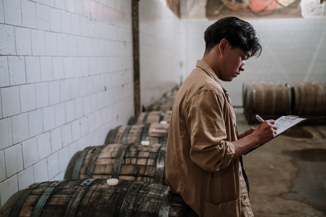 A craft beer expert inspects wooden barrels in a brewery's storage room.